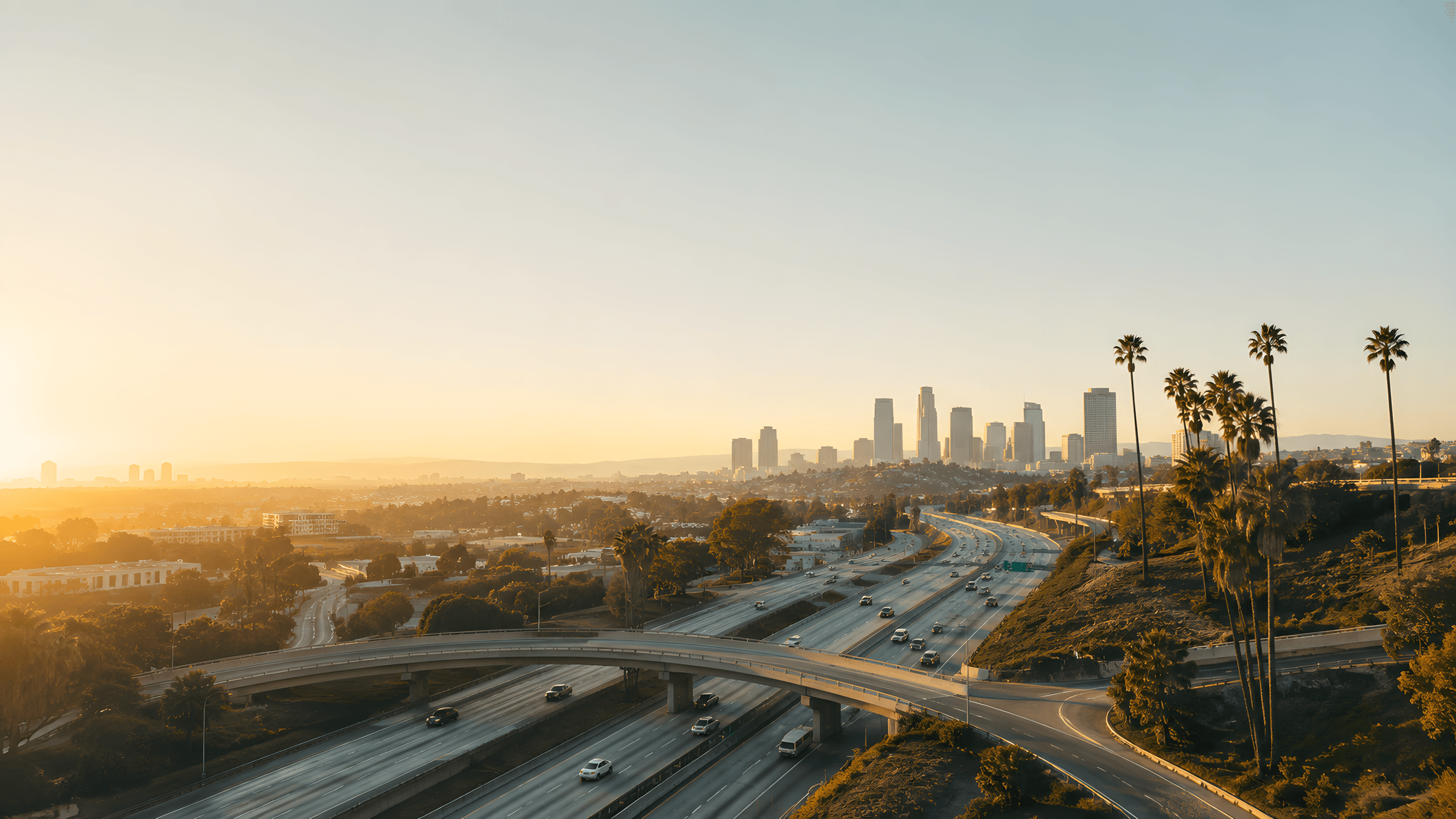 Los Angeles freeway interchange at sunrise with the downtown skyline and palm trees in the distance