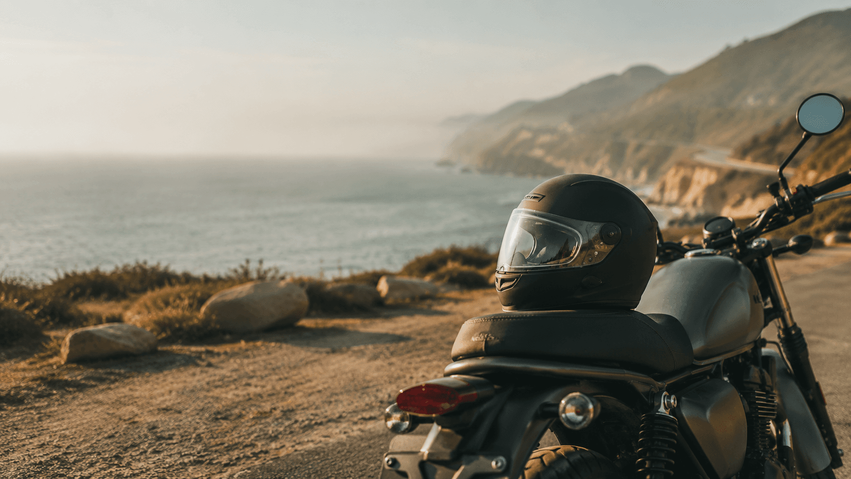 A motorcycle parked on a coastal overlook with a helmet resting on the seat