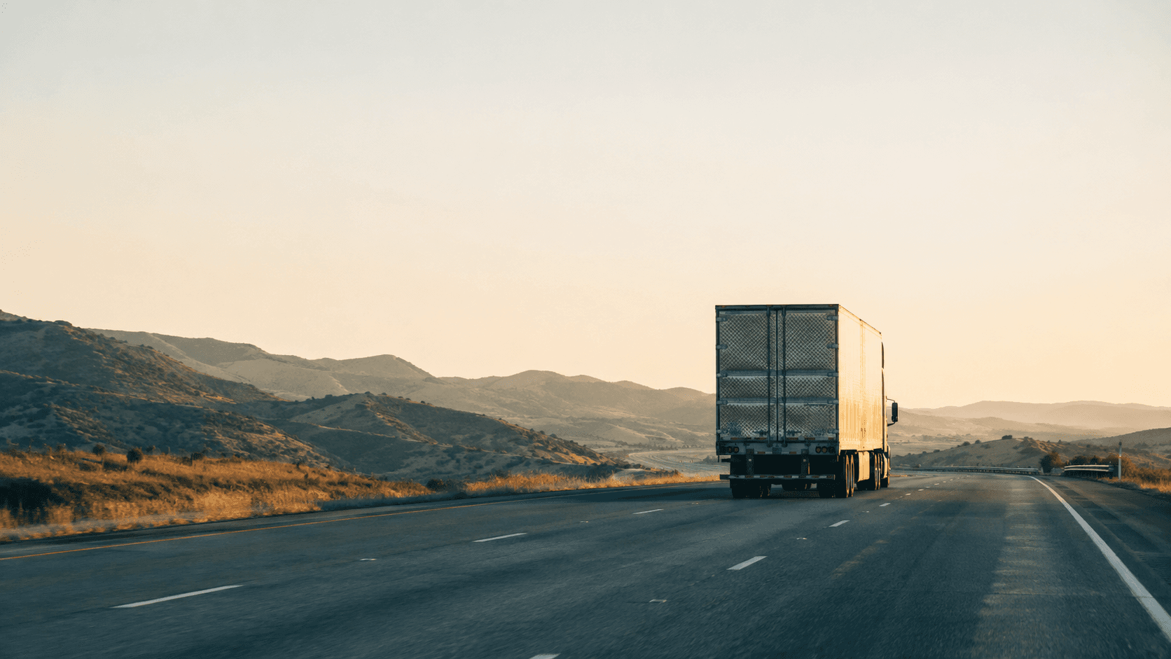 A semi-truck trailer driving away on a California highway through dry hills